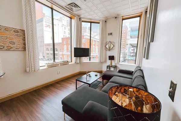 Open-plan vacation rental with dining table, brown sofa, two twin beds, and framed animal artwork on walls